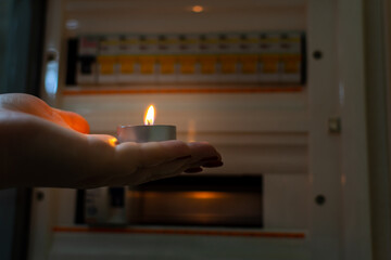 Candle in hand against the background of a meter for electricity