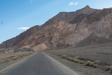 Panoramic view of endless empty road leading to colorful geology of multi hued Artist Palette rock formations in Death Valley National Park near Furnace Creek, California, USA. Black mountains