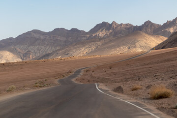 Fototapeta na wymiar Panoramic view of endless empty road leading to colorful geology of multi hued Artist Palette rock formations in Death Valley National Park near Furnace Creek, California, USA. Black mountains