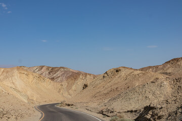 Fototapeta na wymiar Panoramic view of endless empty road leading to colorful geology of multi hued Artist Palette rock formations in Death Valley National Park near Furnace Creek, California, USA. Black mountains
