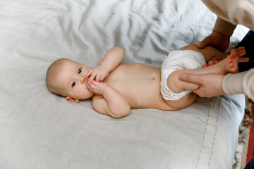 Dad is changing a diaper to a baby on a bed with a beige sheet.