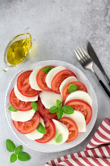 Italian caprese salad with tomatoes, mozzarella, basil, olive oil on a gray background. Italian food.