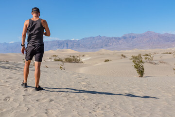 Rear view of man looking at Mesquite Flat Sand Dunes in Death Valley National Park, California, USA. Panoramic view on dry Mojave desert on sunny summer day with Amargosa Mountain Range in the back
