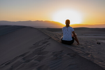 Silhouette of woman enjoying the sunrise with scenic view on Mesquite Flat Sand Dunes, Death Valley National Park, California, USA. Morning walk in Mojave desert with Amargosa Mountain Range in back.