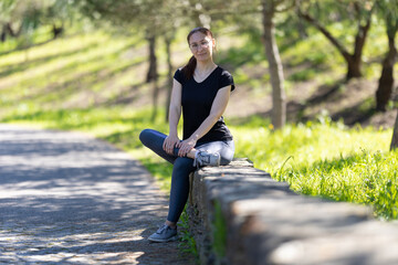 Adult woman in sports clothes sits on the large stone curb and looking in the camera