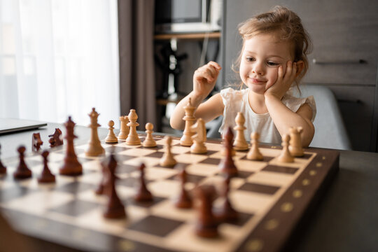 Little girl playing chess at the table in home kitchen. The concept early childhood development and education. Family leisure, communication and recreation.