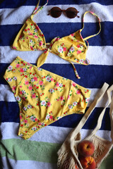 Striped beach towel, floral yellow swimsuit, sunglasses and mesh bag with peaches. Cute beach essentials. Top view. 