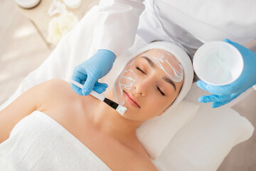 Naklejka premium Skincare Treatment. Cosmetologist Applying Moisturising Mask On Face Of Beautiful Young Woman