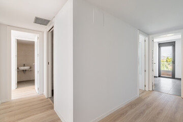View from the corridor to a compact white room, a terrace with a glass door and a bathroom in an unfurnished apartment after renovation. The concept of buying a home with a mortgage