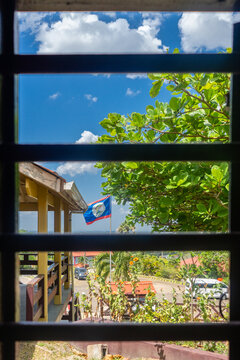 Belize Flag Flying Against Blue Skies in Window View.