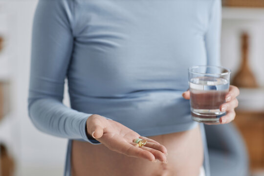Close up of pregnant young woman taking prenatal vitamins and supplements in morning, minimal