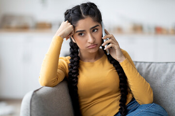 Bored Indian Woman Talking On Cellphone While Sitting On Couch At Home