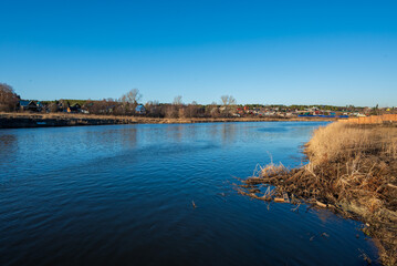 A river with a blue sky and a small town in the background - obrazy, fototapety, plakaty