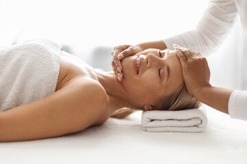 Beautiful middle aged woman getting face lifting massage treatment in spa salon