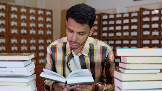 Young indian guy student reading book with serious face in the library. Serious conceived student preparing for an exam