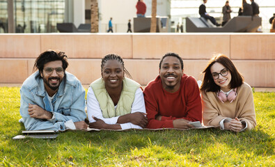 Smiling millennial diverse modern students study together, rest from lesson, lie on grass in university