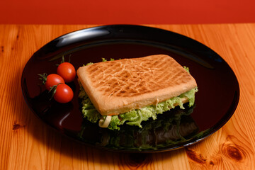 Cooked panini with green lettuce on a black plate with cherry tomatoes.