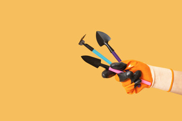 Hand in gardening glove with gardening tools on orange background