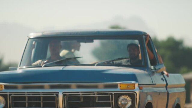 Two women riding in back of pick up truck as friends enjoy road trip through countryside - shot in slow motion