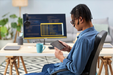 Side view of male IT programmer holding tablet and writing code for mobile devices at workplace