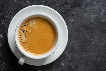 White porcelain coffee cup with saucer over black background, top view, copy space, closeup. Hot coffee in a breakfast