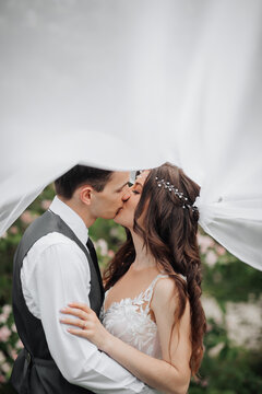 Happy young couple. Wedding portrait. The bride and groom tenderly kiss under a veil against the background of a blooming bush. Wedding bouquet. Spring wedding