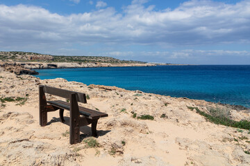 Fototapeta na wymiar A wooden bench by the ocean. Sea with blue water and a rest bench on the shore