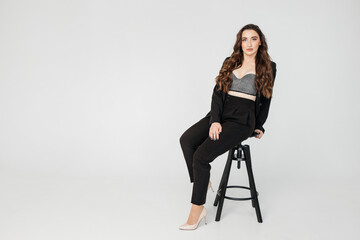 young girl with dark curly hair in a suit sits on a high chair on a white background, copy space