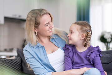 pretty little girl and her mother spending happy sunny morning at home together. mom and daughter looking to each other smiling and cuddling