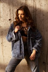 Attractive Latino woman in denim jacket and jeans on grey wall background.