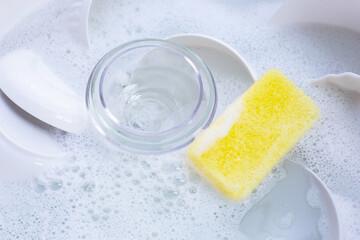 Dishes and bowls with yellow sponge in water and bubbles of dishwashing liquid