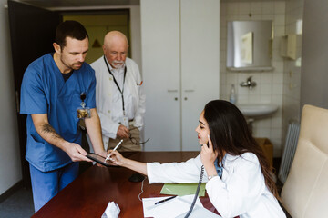 Female doctor talking through telephone while signing on digital tablet held by nurse in office at hospital