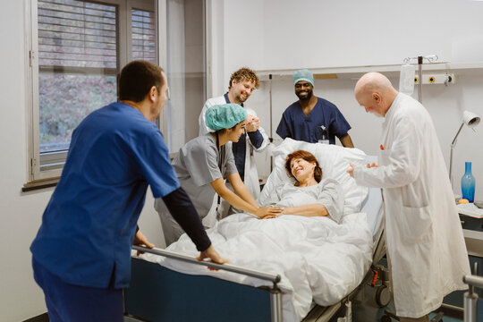 Smiling healthcare workers cheering while standing around senior female patient at hospital