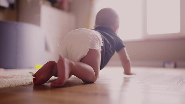 baby learns to crawl on the floor at home. happy family kindergarten kids concept. First steps, baby crawling view from the back. baby learns to crawl to explore dream the world around him