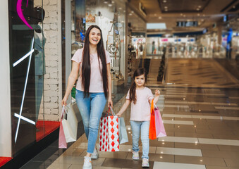 Fototapeta premium young mother and daughter holding shopping bags, shopping in the mall. Family shopping.