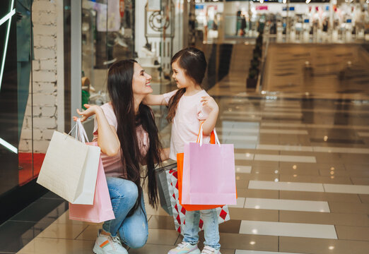 young mother and daughter holding shopping bags, shopping in the mall. Family shopping.