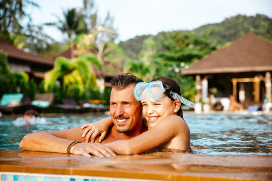 Smiling girl with arm around father in swimming pool at resort during vacation
