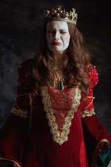 sad medieval queen in red dress with white makeup and crown