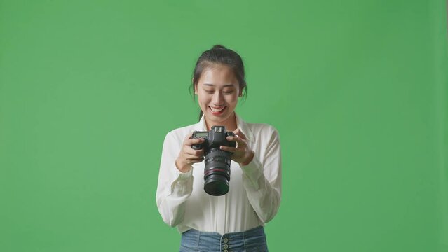Asian Photographer Taking Pictures Then Looking At Them In The Camera While Standing On Green Screen Background In The Studio
