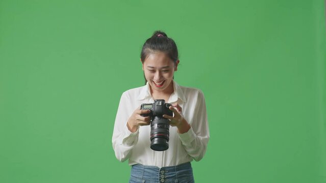 Asian Photographer Looking At The Pictures In The Camera Then Screaming Goal Celebrating Satisfied With Her Work While Standing On Green Screen Background In The Studio
