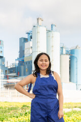 Happy young woman in blue overalls standing cheerfully against background of factory