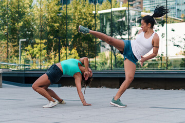 mujeres practicando patadas, ejercicios y capoeira en la ciudad. entre edificios con reflejos en un día soleado.