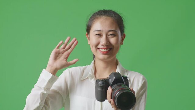 Close Up Of Asian Photographer Looking At The Pictures In The Camera Then Waving Her Hand While Standing On Green Screen Background In The Studio
