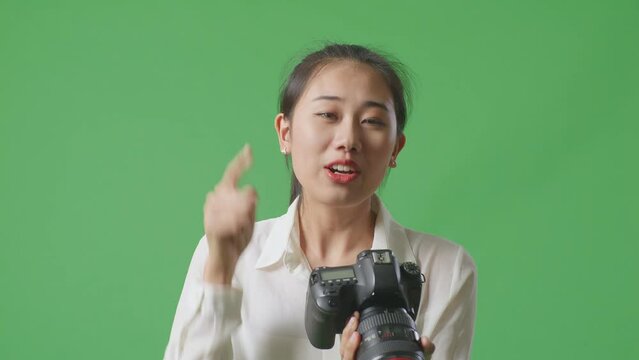 Close Up Of Asian Photographer Looking At Pictures In The Camera And Shaking Her Head Being Unsatisfied With The Result On Green Screen Background In The Studio
