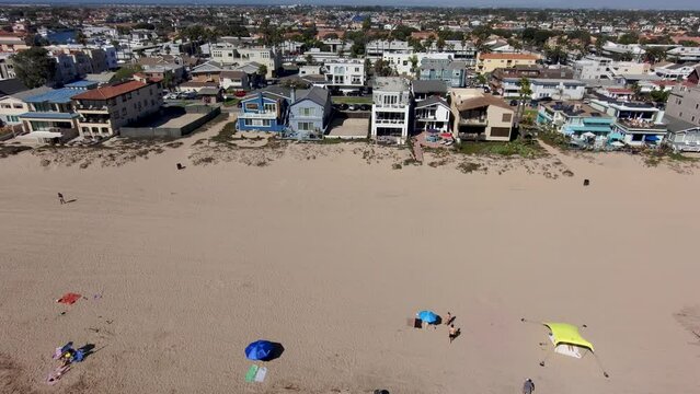 sideways aerial footage along the coastline at Rosie's Dog Beach with people walking along the beach and laying in the sand and beachfront homes and apartments with blue sky in Long Beach California