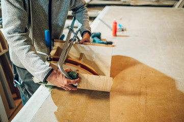 Close up of a carpenter using clamps for joining furniture parts in his workshop.