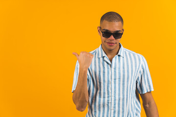 Afro-American boy with sunglasses pointing thumb aside at blank space, medium shot, orange background, copy space. High quality photo © PoppyPix