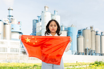 Sad young woman holding big flag of China against background of factory