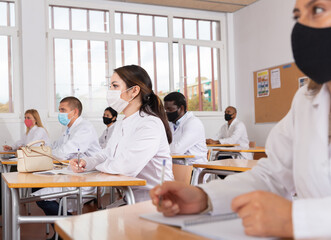 Woman studying in classroom with colleagues medicals in protective face masks for disease prevention during training program for health workers