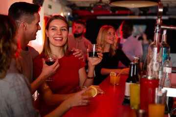 Happy cheerful positive smiling woman and man joying in the night club with drinks in the hand. High quality photo